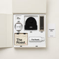 The Roast. founder gift box — light Apple-unboxing flat-lay: wordmark pin, Hot Take mug, Receipts Included beanie, hot take pencils, canvas tote, white water bottle, and an I support you. card.